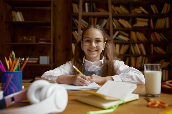 幸せな女子高生の肖像画は宿題をするか 自宅の図書館で机で勉強する ホームスクーリングコンセプト — ストック写真