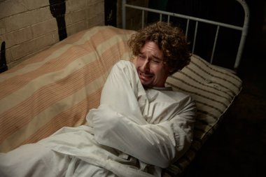 Deli gömleği giymiş deli bir adam hastane yatağında ağlıyor ve çığlık atıyor. Klinik Psikiyatri Bölümü 'nün hastası delilik krizi geçiriyor.