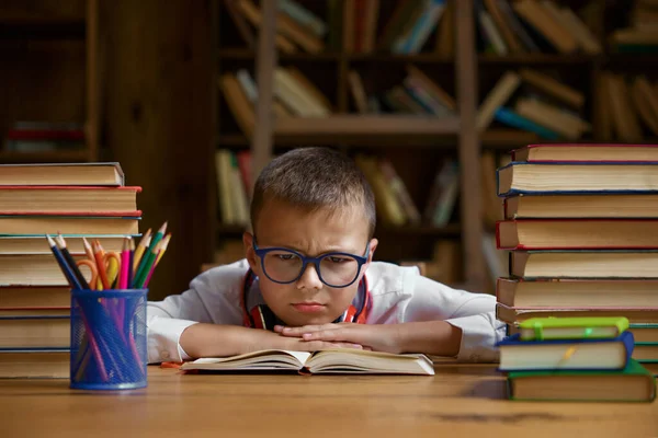 机のテーブルに座り たくさんの教科書を積み重ねている絶望的な子供 オンライン学習の問題と宿題の困難 — ストック写真