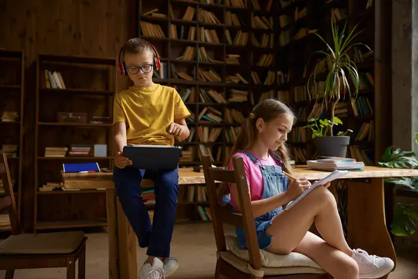 Brother and sister schoolchildren studying at home together. Little boy trying to see what her sibling writing in diary. Family relationships between children concept