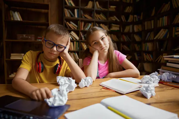 疲れ果てた子供たちは 崩壊した紙の束でテーブルに座って宿題をすることはできません オンライン教育や宿題に苦労している小さな兄弟姉妹 — ストック写真