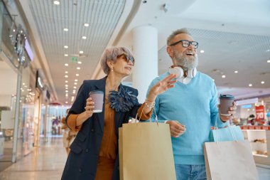 Modaya uygun yaşlı bir çift, hafta sonları alışveriş turunun keyfini çıkarıyor. Emekli olan mutlu yaşlı adam ve kadın alışveriş merkezinde yeni moda kıyafetler seçiyor.