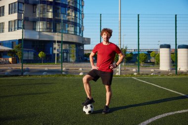 Futbol sahasında ayakta duran futbol topuna basan genç bir adamın portresi. Açık havada en sevilen oyun alıştırması