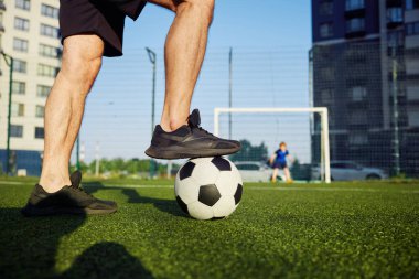 Aile sahada futbol oynuyor. Baba ayağının futbol topuna odaklan. Baba gol atmaya hazırlanıyor, evlat kapıyı koruyor.