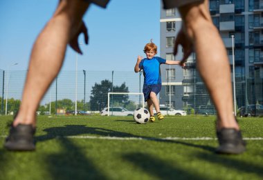 Baba oğul, şehir stadyumunda aile futbol yaz kampı düzenliyor. Çocuk tekme atarken babanın topu yakaladığı yakın çekim.