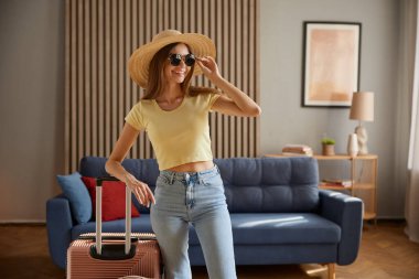 Seyahate çıkan genç bir kadın, tatil tatili başlangıcı, tatil gezisinin başlangıcı. Hasır şapka ve güneş gözlüğü takıp valizlere poz veren muhteşem bir kadın.
