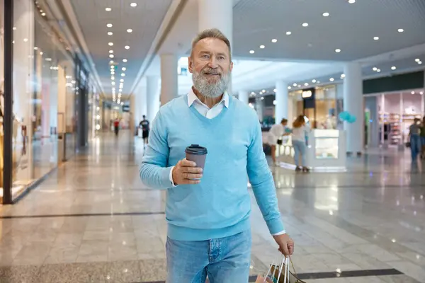 Handsome senior man going shopping at store. Smiling aged businessman feeling satisfaction with great discount at airport retail place