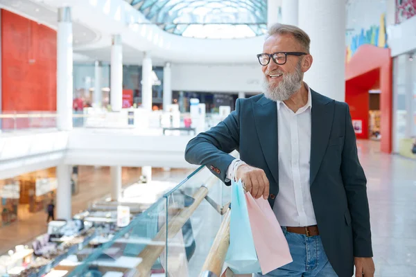 Happy smiling senior businessman at showcase in shopping mall. Confident mature male buyer rejoicing special discount offer and gift bonus for purchase at retail place. Vip client at supermarket