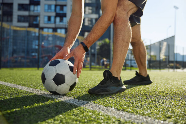 Start football match. Male player putting ball on strip line on center of soccer field cropped closeup shot