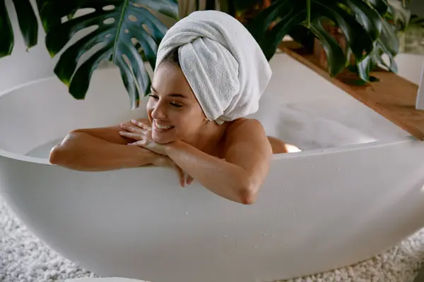 Relaxed woman wearing towel on head bathing having leisure time at home. Natural cosmetics for body treatment and spa routine