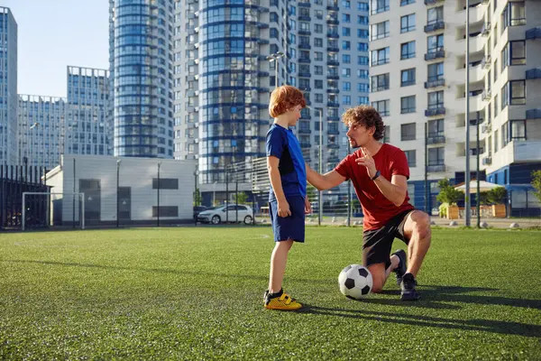 父親は息子にシティスタジアムでサッカーをするように教えています パパは サッカーボールをキックする方法を少年に話す スポーティブな家族のレクリエーション ストック写真