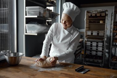 Mutfakta hamur işi ya da hamur işi hazırlamak için üniforma giyen mutlu ve genç bir fırıncı. Fırın kavramı
