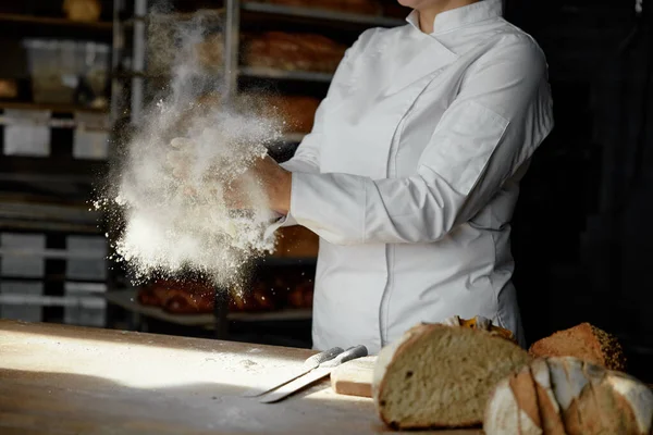 Closeup female chef hands clapping in cloud of powdery flour over table freeze motion. Culinary process