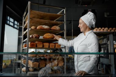 Küçük işletme sahibi yerel bir girişimci. Gülümseyen genç kadın fırıncı raftan ekmek alıyor.