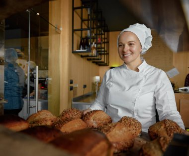Lezzetli taze ekmek sunan neşeli fırıncı bayanın portresi. Ev yapımı organik ürünler küçük endüstri konsepti