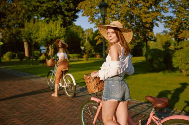 Halk parkında bisikletle yürüyen iki güzel kız en iyi arkadaş. Çekici bir bayan çiçekçi. Birbirine eşlik ediyor.