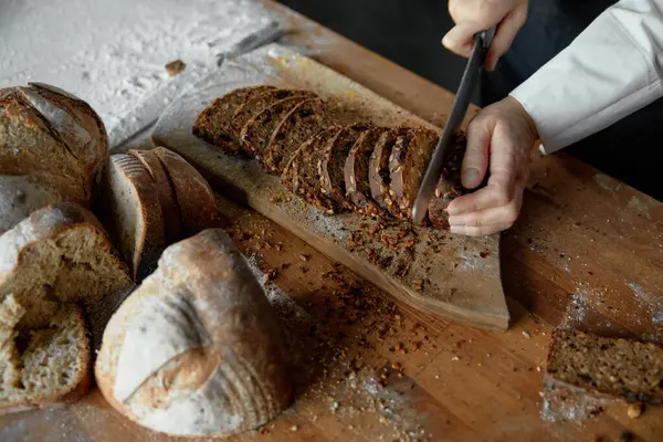 Closeup middle section woman chef cutting crispy crust yeast-free sourdough bread into slices. Pastry shop concept