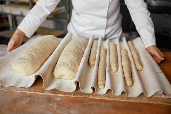 Woman baker making fresh bread in local bakery. Female pastry cook holding tray with raw loaf dough. Food business concept