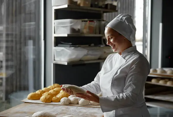 Experienced skilled woman baker forming baguettes working in bakery. Female chef shaping bread from raw dough. Professional breadmaking service