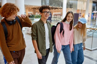 Alışveriş merkezinde farklı mağazalarla yürüyen mutlu bir grup çocuk. Erkekler ve kızlar boş vakitlerinde yeni bir eğlence arıyorlar.