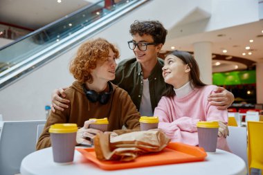 Alışveriş merkezinde yürüyüş sırasında fast food atıştıran ve kafelerde içki içen genç arkadaşlar. Gençler arasında dostça bir sohbet.