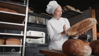 Gülümseyen kadın fırıncı taze pişmiş ekmeği kontrol ediyor. Pastane çalışanı.