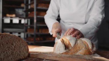 Kadın aşçı fırın mutfağında tahta tahtada sağlıklı ekmeği dilimliyor. Üretim hattında kalite kontrolü