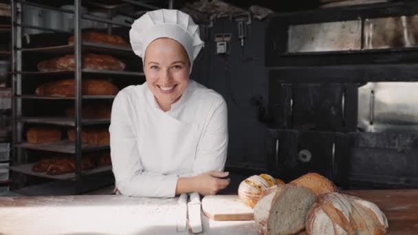 カメラを見ているユニフォームを着て笑顔でハッピーな女性シェフベイカー ベーカリーキッチンでプロの料理 — ストック動画