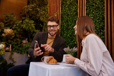 Genç bir adam ve kadın cep telefonu kullanarak kafede iş görüşmesi yapıyorlar. Sosyal medya ağlarını izleyen kaygısız iş adamları iş molasında rahatlatıcı anın tadını çıkarıyorlar.