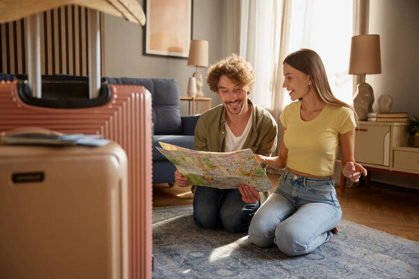 Preparation for vacation concept. Focus on packed luggage suitcases with happy spouses searching travel rout in paper map on blurred background
