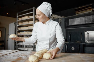 Dişi fırıncı fırında pişirmeden önce çiğ çörek hazırlıyor. Endüstriyel fabrika kavramı. Doğal gıda üretimi.