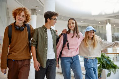 Alışveriş merkezinde farklı mağazalarla yürüyen mutlu bir grup çocuk. Erkekler ve kızlar boş vakitlerinde yeni bir eğlence arıyorlar.