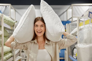 Genç bayan müşteri kumaş mağazasından alışveriş yapıyor. Mutlu kadın portresi. Elinde iki yastıkla kameraya bakıyor.