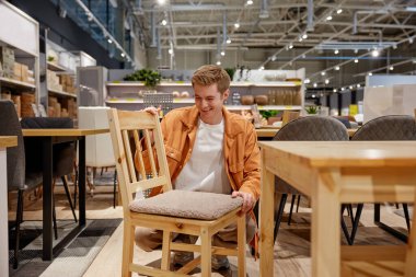 Delikanlı mobilya deposunda yeni bir sandalye arıyor. Yakışıklı adam ev eşyaları sergisini ziyaret ediyor.