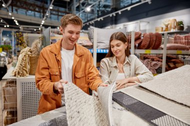 Heyecanlı erkek ve kadın çift mağazada ev dekorasyonu için döşeme paspası seçiyor. Alışveriş zamanı etkinliği