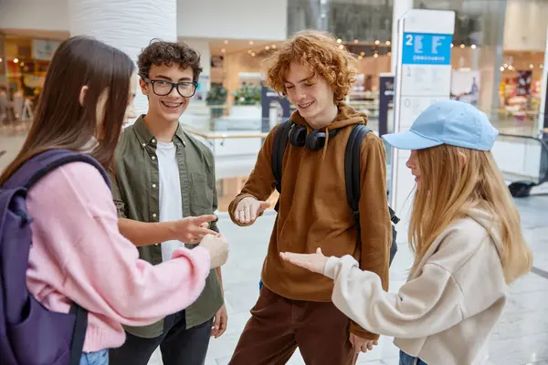Teenagers friends playing rock-paper-scissors hand game while standing in hall of big shopping mall