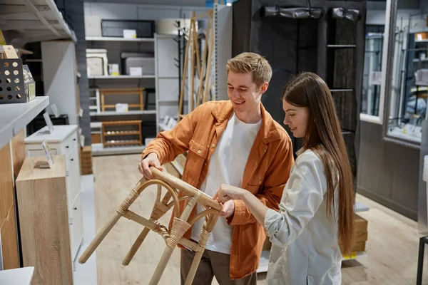 Markette hasır sandalyeli bahçe mobilyalarını izleyen genç bir çift. Alışveriş heyecanı ve tüketim konsepti