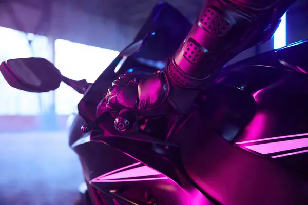 Motor biker wearing protective suit driving sport motorcycle in neon light and smoke. Indoor motordrome for speed riding practice