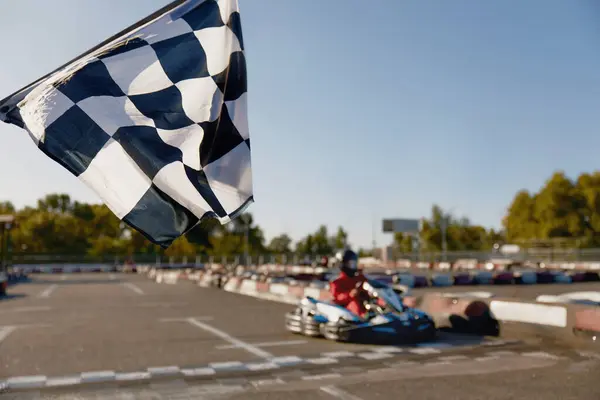 Go-kart driver crossing at finish line moving to checkered racing flag. Active battle win for first place in extreme auto sports championship