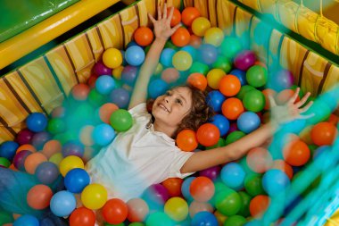 Çok renkli plastik topla dolu havuzda oynayan mutlu çocuk. Heyecanlı neşeli çocuk, oyun odasındaki kuru havuzlarda eğleniyor.