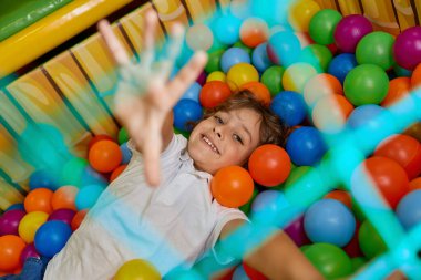 Çok renkli plastik topla dolu havuzda oynayan mutlu çocuk. Heyecanlı neşeli çocuk, oyun odasındaki kuru havuzlarda eğleniyor.