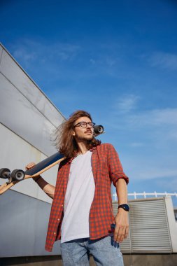 Şehrin arka planında omzunda uzun panosu olan mutlu bir hippi. Ekstrem spor, gençlik kültürü kavramı