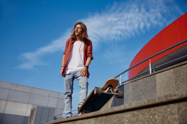 Şehrin caddesinde kaykay yapan enerjik, stil sahibi bir hippi. Ciddi, genç, sportif, sıradan bir adam. Uzun panodaki aşırı ırkın tadını çıkarıyor.