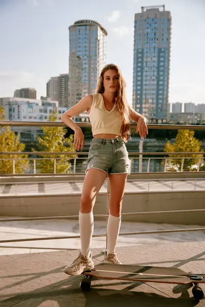Havalı hippi kadın kaykaycı şehir manzarası üzerinde uzun panosuyla poz veriyor. Güzel, sportif bir genç kız şehir merkezinde antrenman yapıyor. Gençlik kültürü ve spor konsepti