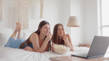 Heyecanlı genç kız arkadaşlar ya da kız kardeşler dizüstü bilgisayarda komik filmler izleyip yatak odasında patlamış mısır yiyorlar. Pijama partisi konsepti