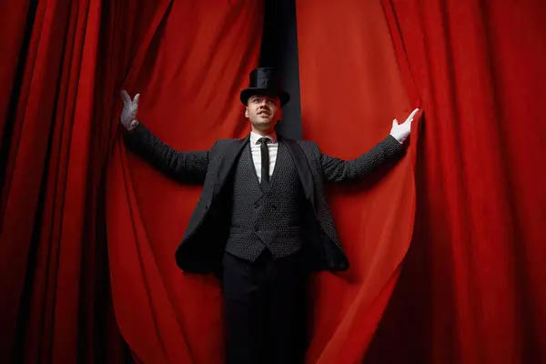 Cinematic posed portrait of magician actor over red velvet stage curtain. Magic entertainment presentation with unexpected illusionist performer entrance and appearance
