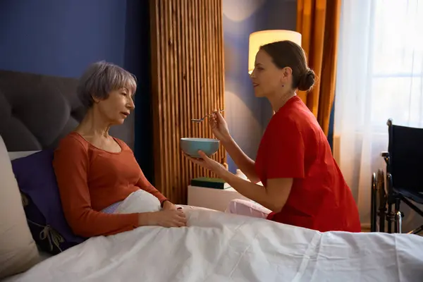 女护士在家里的卧室里喂老年妇女 提供私人护理服务的女性护理专家 — 图库照片