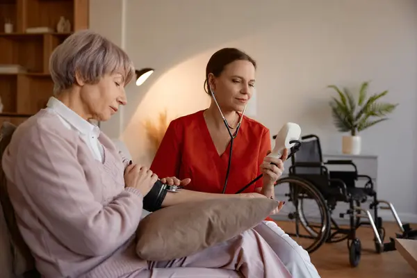 注意深い女性医療従事者は デジタルテノメーターを使用して 老人ホームや退職後の家のアパートで高齢女性患者の血圧を取ります 心臓検査サービス — ストック写真