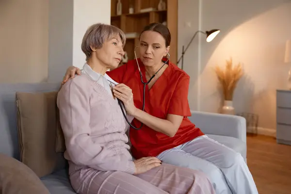 女性医師は 介護施設で高齢女性を診察しながら ステススコープを使用しています 退職後の高齢者のためのプロフェッショナルヘルスケアの身体検査 — ストック写真
