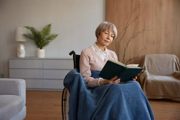 坐轮椅看书的残疾退休妇女 老年妇女在家里或疗养院度过闲暇时间 防止老年人痴呆症的休闲活动 — 图库照片
